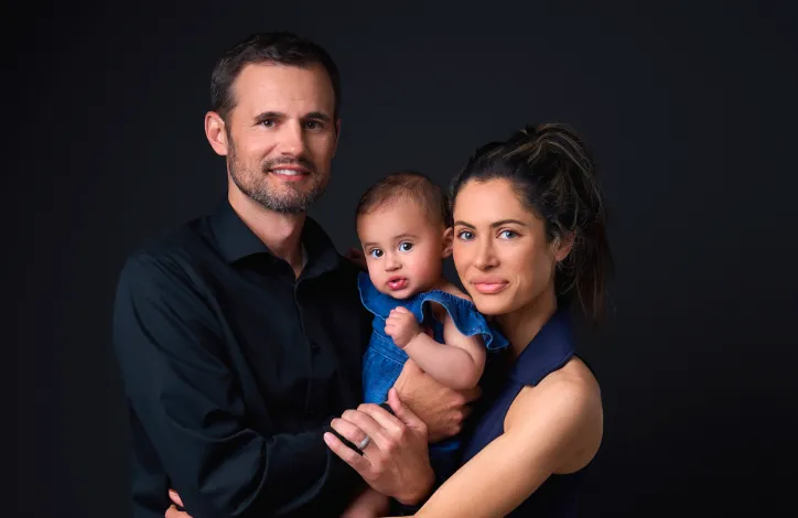 Professional portrait of a man, woman, and baby against a dark background.