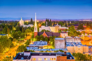 Aerial view of a cityscape at dusk with illuminated buildings and a prominent church steeple.