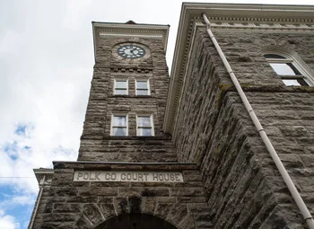 Stone facade of Polk County Courthouse with clock tower against cloudy sky.