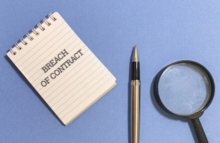 Spiral notebook with "BREACH OF CONTRACT" text, black and gold pen, and magnifying glass on blue surface.