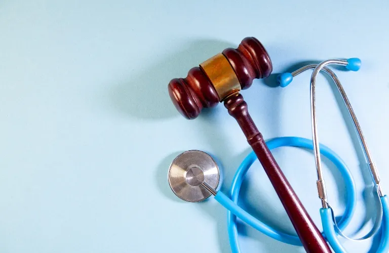 Wooden judge's gavel and blue stethoscope on light blue background.