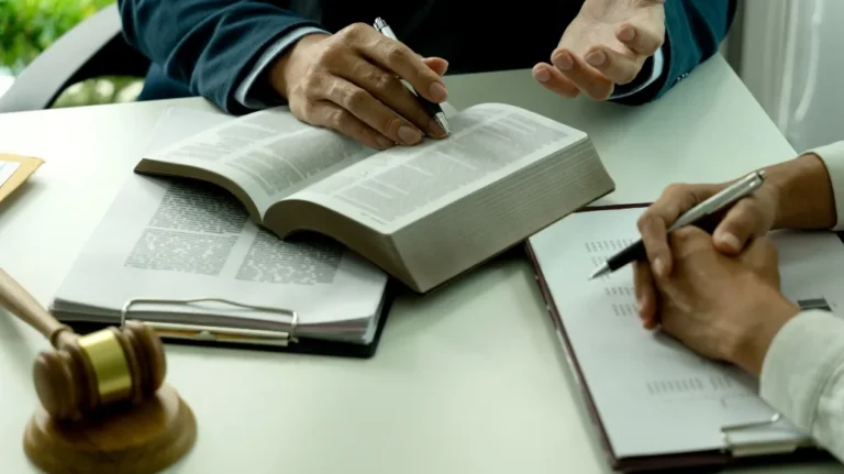 Two individuals discussing legal documents with an open book and gavel on white table.