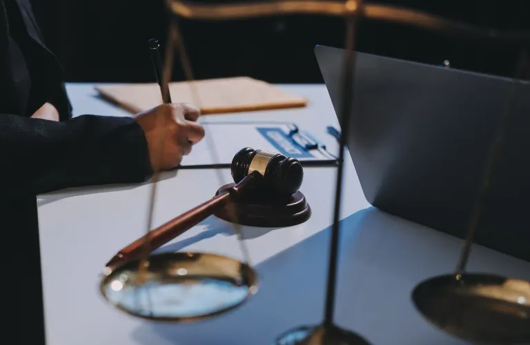 Close-up of a judge's gavel, scales of justice, and a person writing at a desk with a laptop.