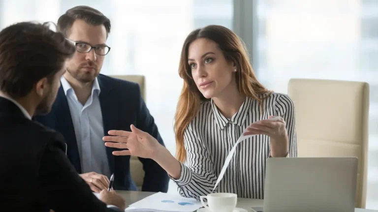Three professionals engaged in a discussion around a table with documents and a laptop.
