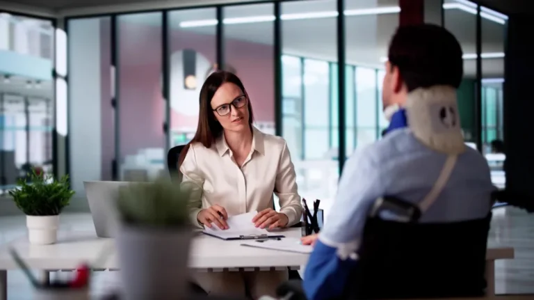 Professional woman in white blouse conducting an office meeting with injured man wearing a neck brace.