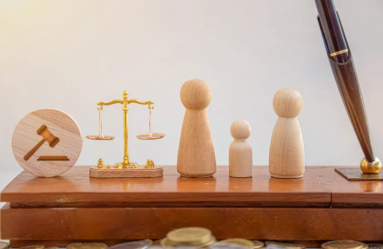 Wooden gavel symbol, golden scales of justice, three wooden figurines, and a pen on wooden surface.