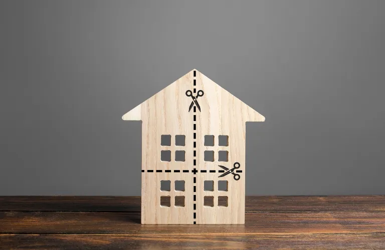 Wooden house model with black dashed cut lines and scissor icons on gray background.