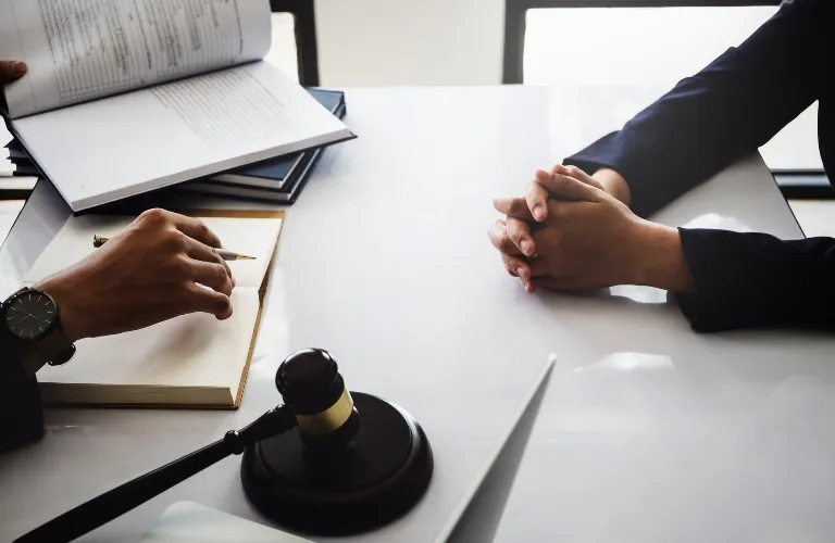 Two individuals seated at a table with legal documents, a gavel, and a laptop.
